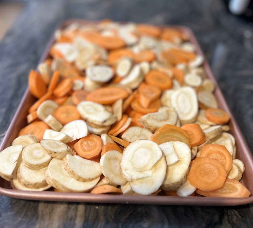 Thinly sliced carrots and parsnips spread onto baking sheet